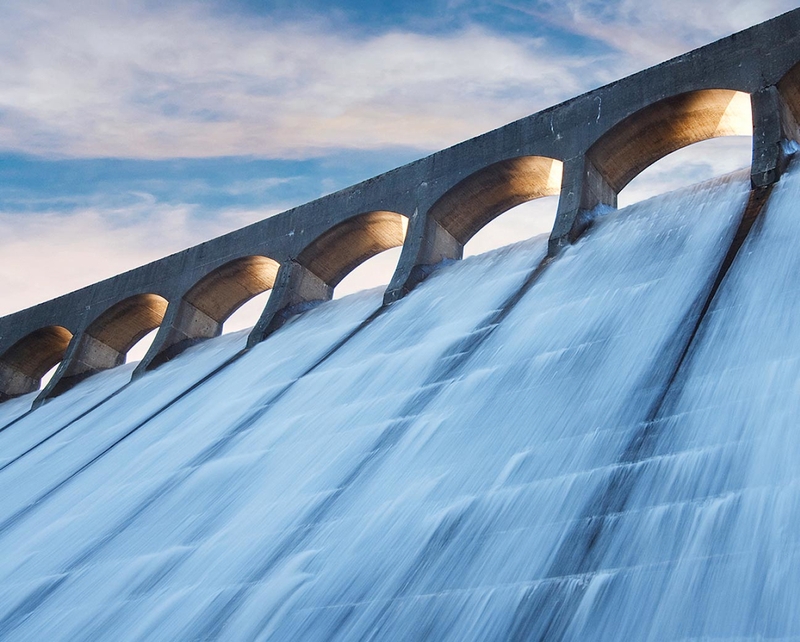 Wasser strömt von einem Damm herunter im Abendlicht.